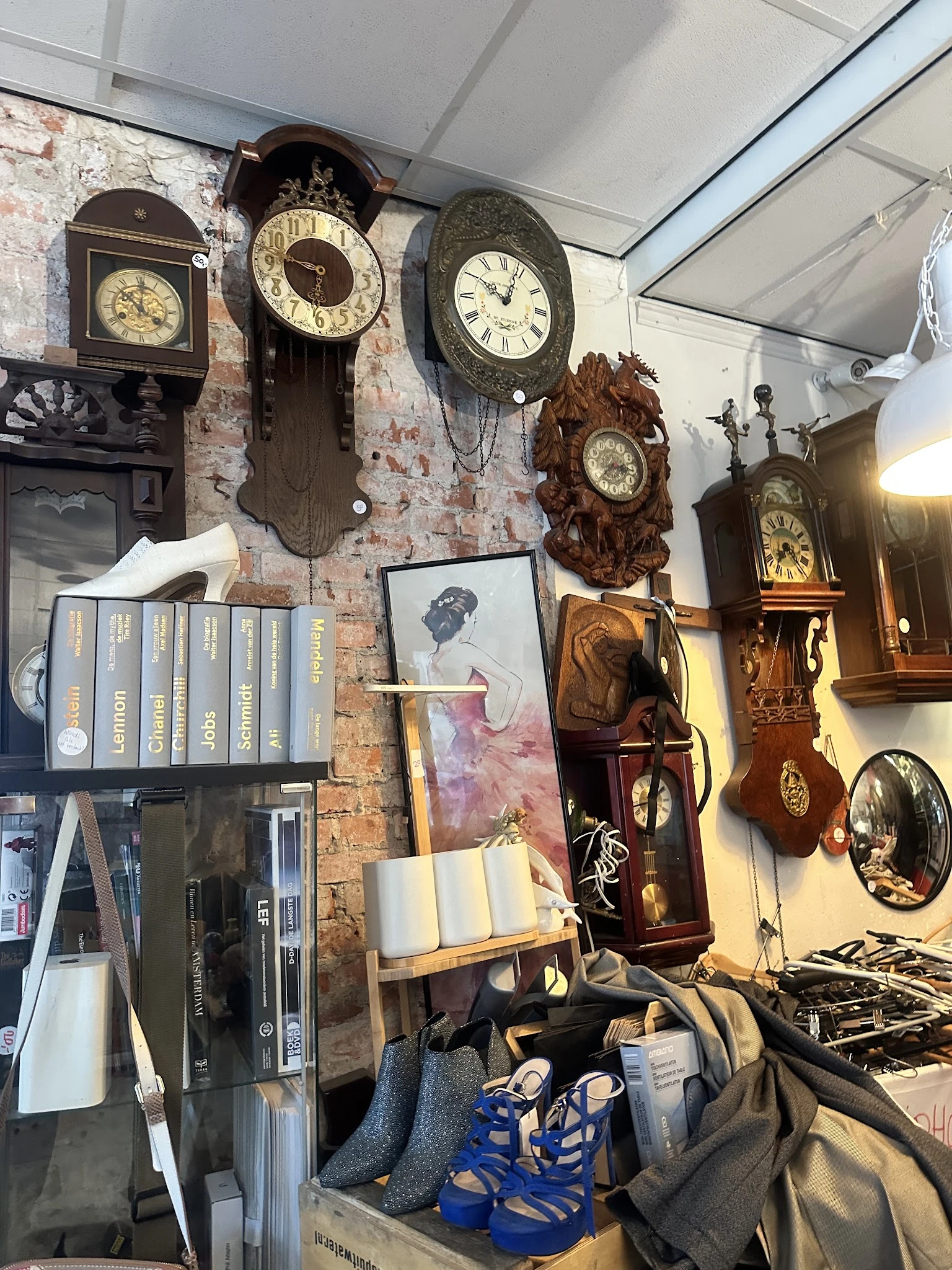 Diverse gebruikte artikelen aan muur: vintage klokken, schilderijen, boeken en decoratieve items