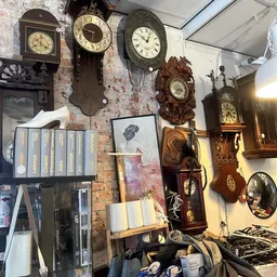Diverse gebruikte artikelen aan muur: vintage klokken, schilderijen, boeken en decoratieve items