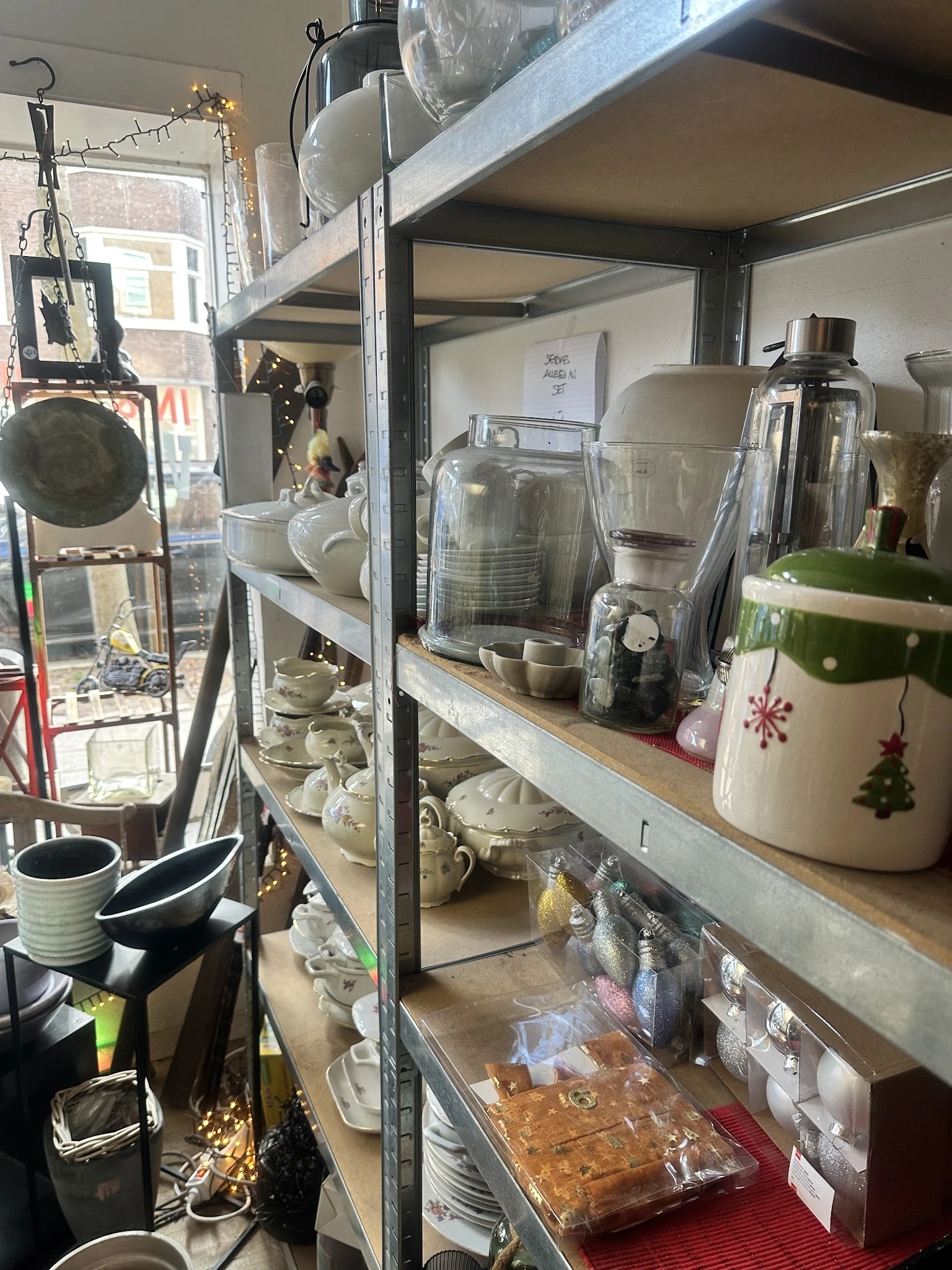 Glazen kasten met huishoudelijke artikelen: blenders, kopjes, servies en keukengerei in een kringloopwinkel
