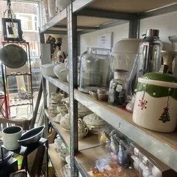 Glazen kasten met huishoudelijke artikelen: blenders, kopjes, servies en keukengerei in een kringloopwinkel