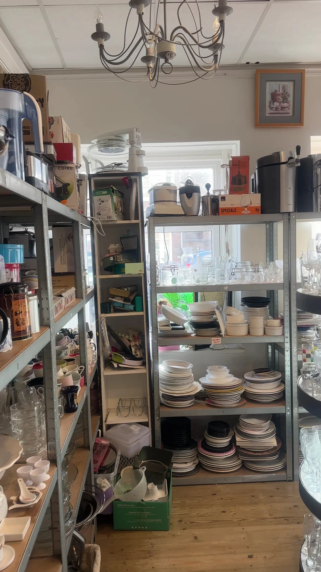 Metalen stellingen met stapels serviesgoed, borden, kopjes en huishoudelijke items in een kringloopwinkel