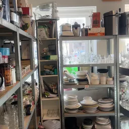 Metalen stellingen met stapels serviesgoed, borden, kopjes en huishoudelijke items in een kringloopwinkel