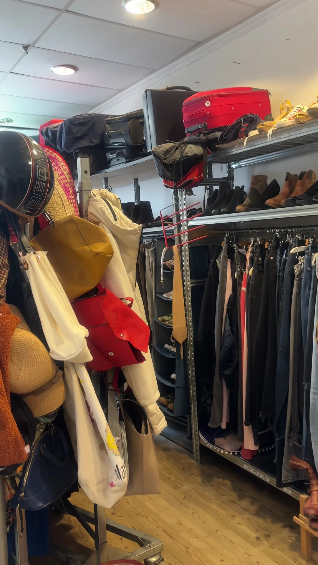 Rekken met tweedehands kleding, waaronder gele en rode kledingstukken op hangers in de kringloopwinkel