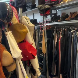 Rekken met tweedehands kleding, waaronder gele en rode kledingstukken op hangers in de kringloopwinkel