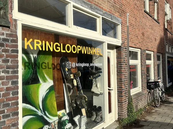 Winkelfront met grote gele letters 'KRINGLOOPWINKEL' en etalage met tweewielers en andere goederen