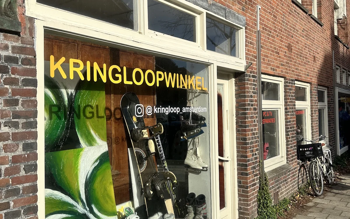 Winkelfront met grote gele letters 'KRINGLOOPWINKEL' en etalage met tweewielers en andere goederen