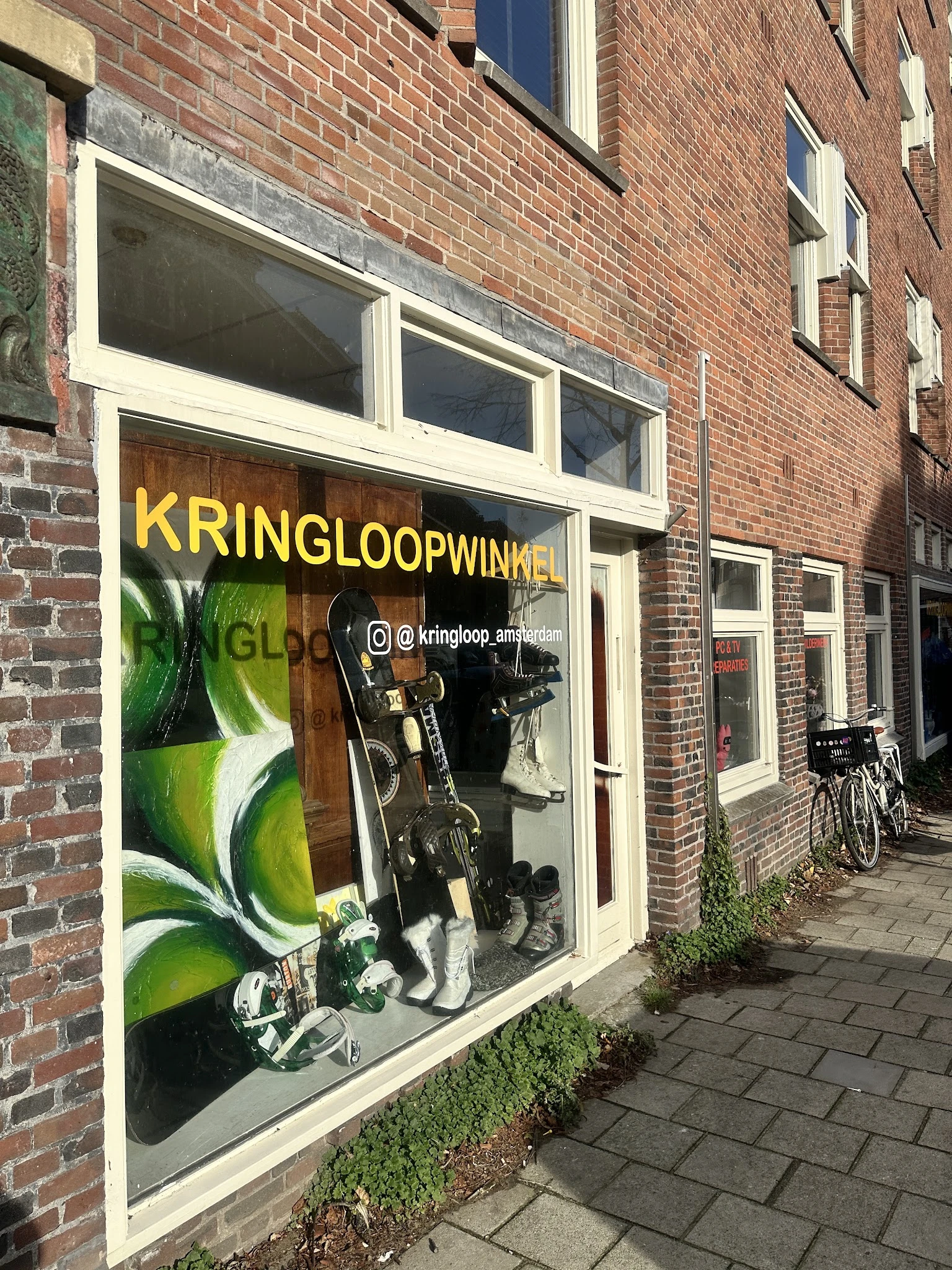 Winkelfront met grote gele letters 'KRINGLOOPWINKEL' en etalage met tweewielers en andere goederen