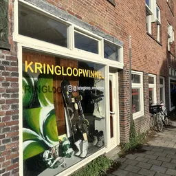 Winkelfront met grote gele letters 'KRINGLOOPWINKEL' en etalage met tweewielers en andere goederen