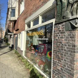 Winkelgevel met gele letters 'KRINGLOOP WINKEL' op raam, uitstallingen met spullen zichtbaar, bakstenen gevelbekleding