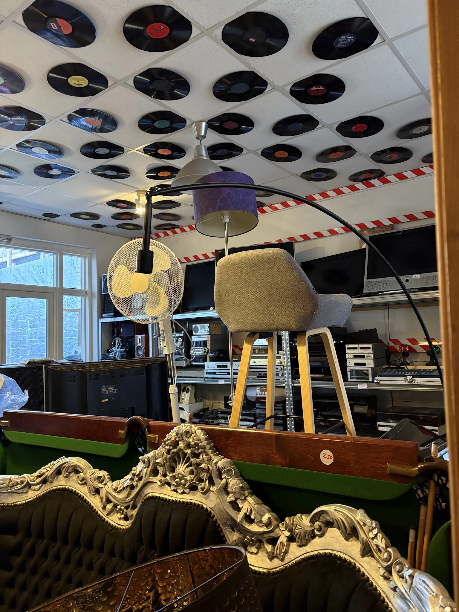 Gele vintage stoel met zwarte poten en hangende lamp tegen plafond met vinyl records