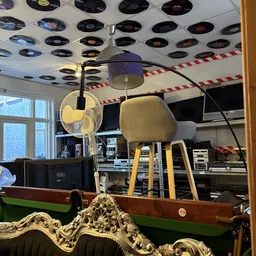 Gele vintage stoel met zwarte poten en hangende lamp tegen plafond met vinyl records
