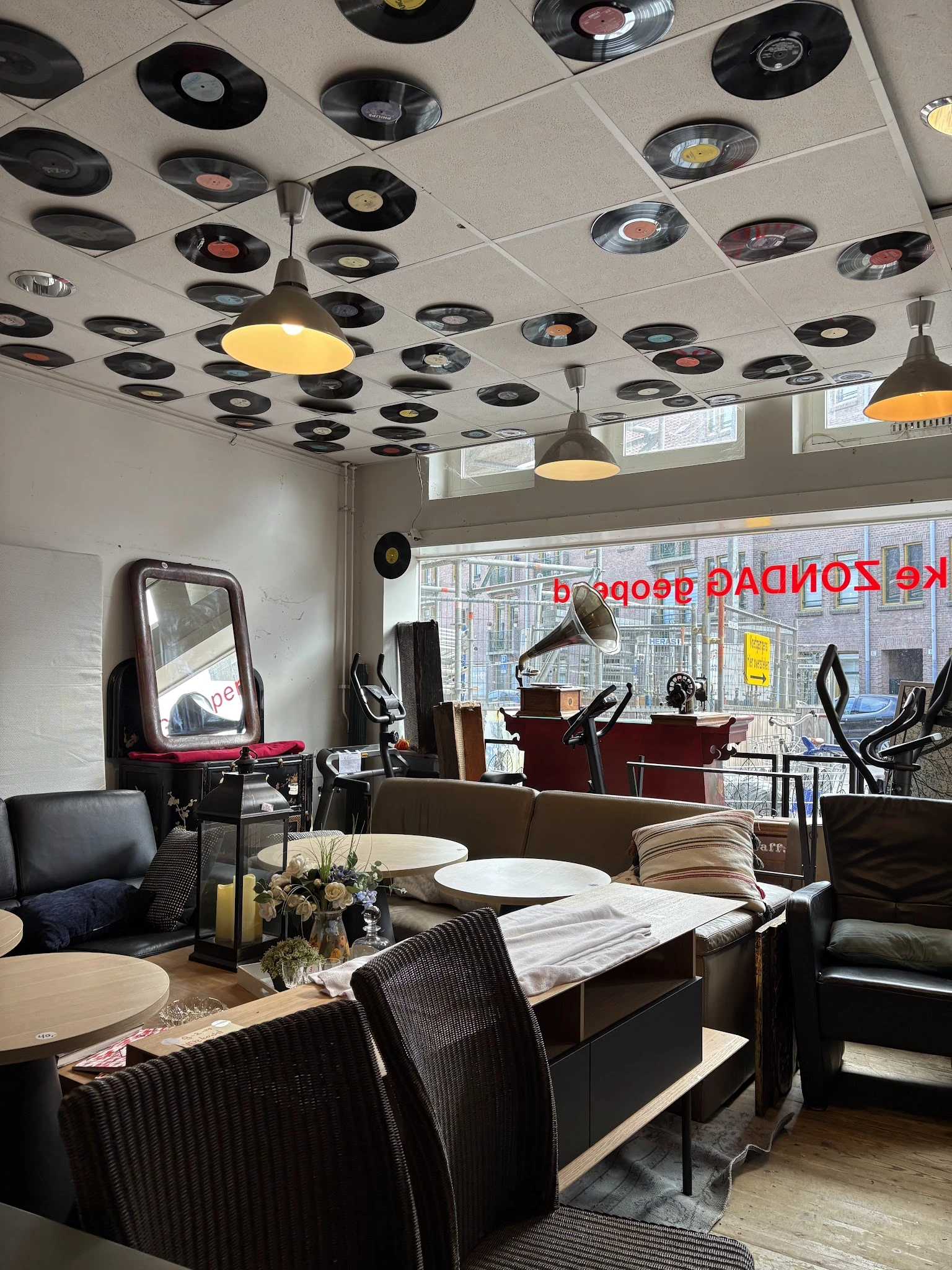 Interieur van kringloopwinkel met meubels, spiegels, lampen aan plafond en uitzicht op straat