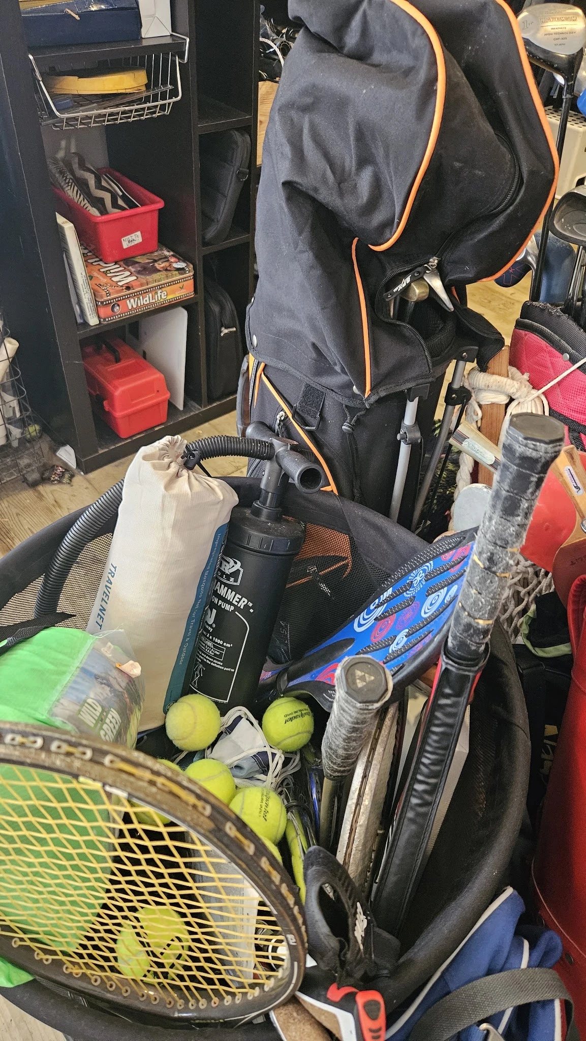 Verzameling sportartikelen waaronder tennisracketten, golfballen en diverse tassen in een kringloopwinkel