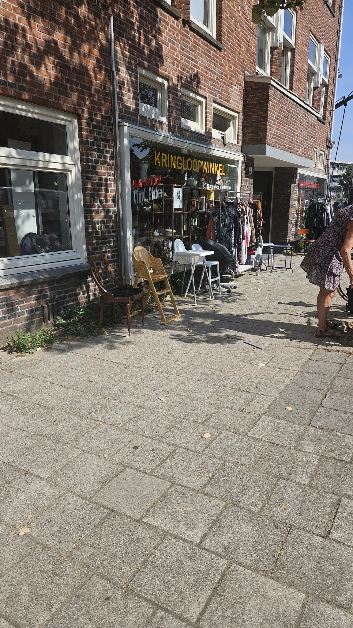 Winkelterras met stoelen en tafels langs een bakstenen gevel, met kledingrek op de achtergrond