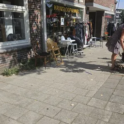 Winkelterras met stoelen en tafels langs een bakstenen gevel, met kledingrek op de achtergrond