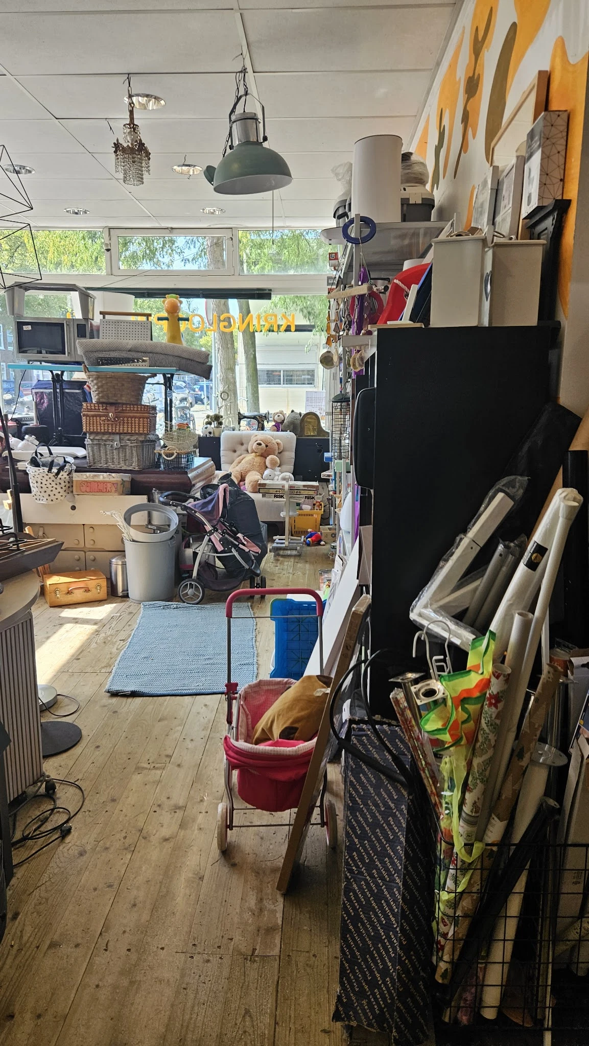 Overzicht van kringloopwinkelinterieur met diverse tweedehandsartikelen op de vloer en stellingen