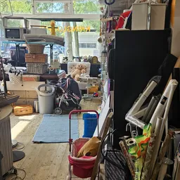 Overzicht van kringloopwinkelinterieur met diverse tweedehandsartikelen op de vloer en stellingen