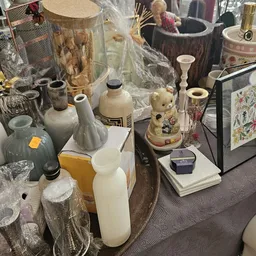 Uitgestalde tweedehands huishoudartikelen en decoratiestukken waaronder vazen, kandelaars en keramische items op toonbanken