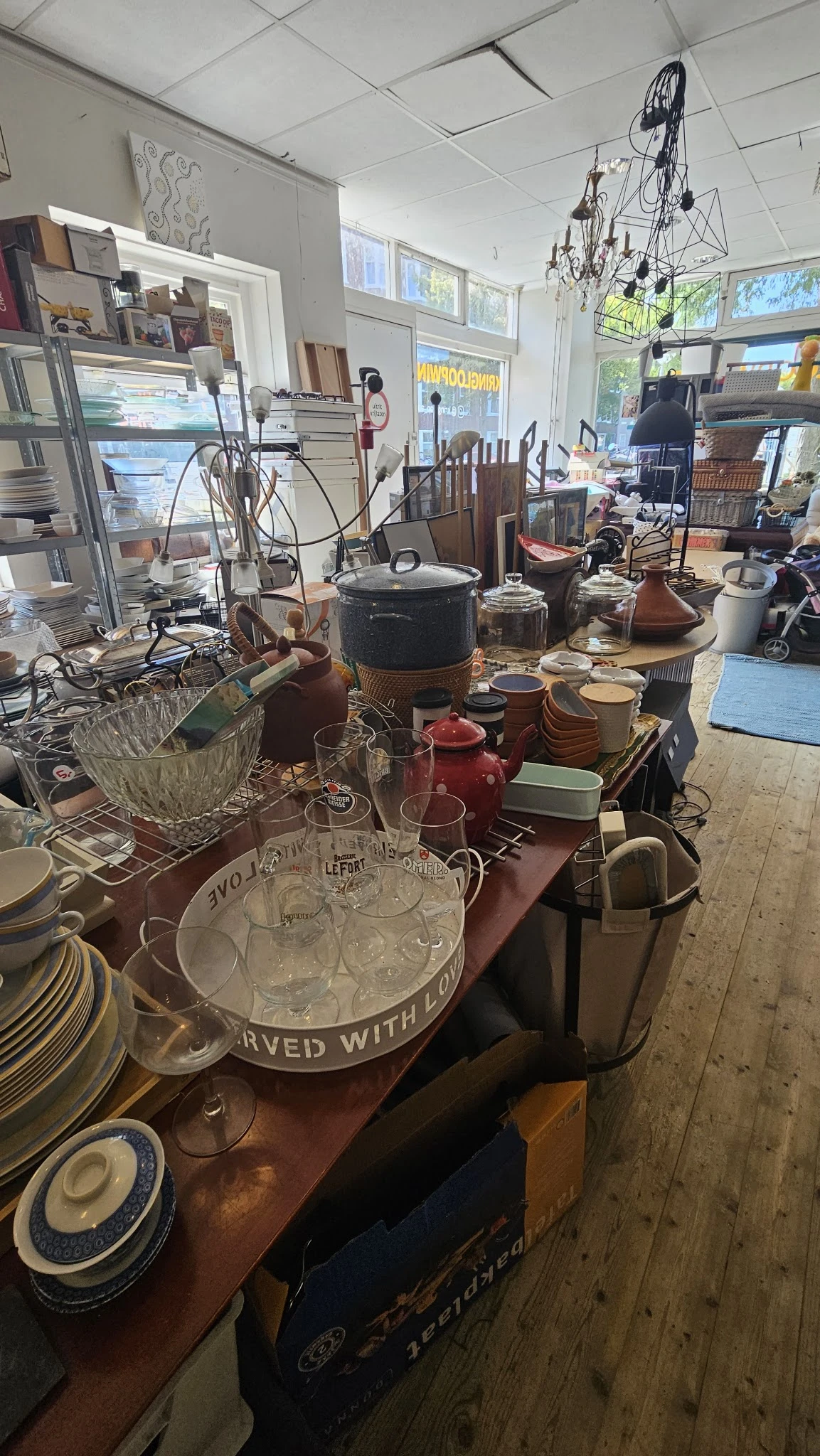 Tafel vol met serviesgoed, glazen, ketels en huishoudelijke spullen in kringloopwinkel