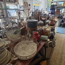 Tafel vol met serviesgoed, glazen, ketels en huishoudelijke spullen in kringloopwinkel