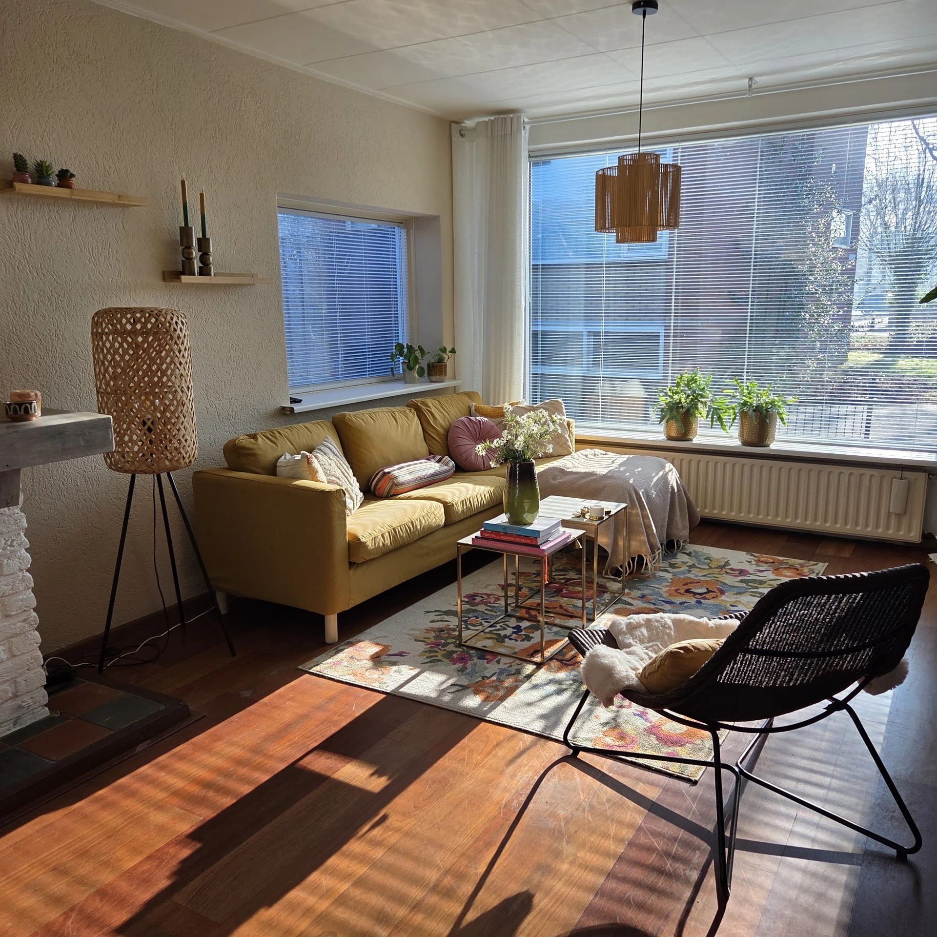 Verzorgd winkeltafereel met gele bank, zwarte fauteuil, salontafel en plantjes bij grote ramen