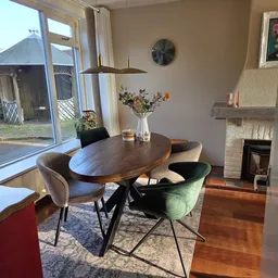 Ovaal houten eettafel met zwart onderstel en groene en grijze stoelen in een huiskamer