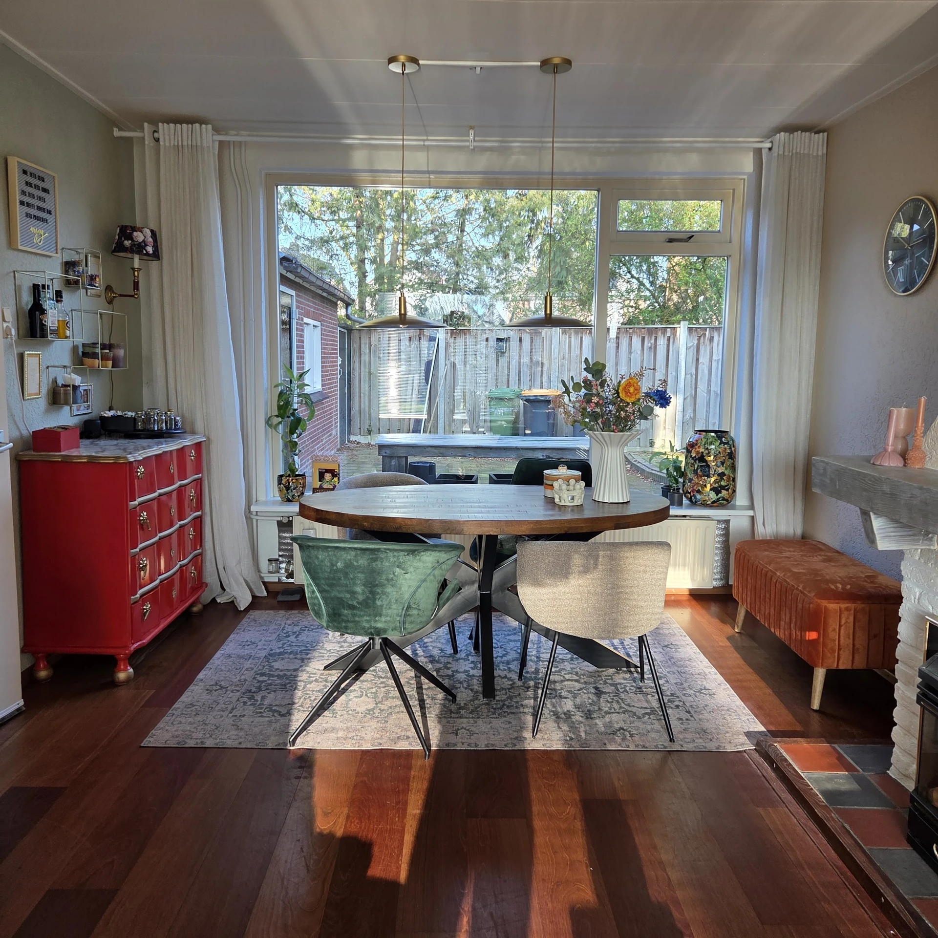 Ronde houten eettafel met groene en crèmekleurige draaistoelen in een interieur bij een raam