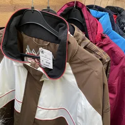 Uitgestalde tweedehands jassen en jasjes in verschillende kleuren met prijskaartje van 19,50 euro