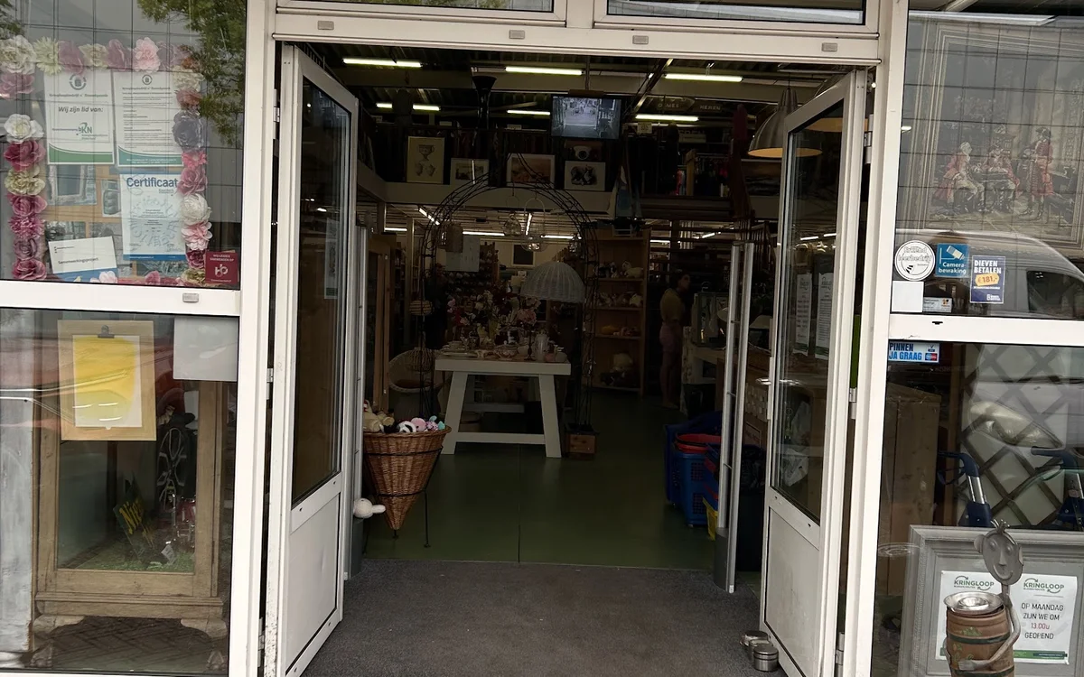 Entreepui van kringloopwinkel met openstaande deuren en uitzicht op winkelinterieur
