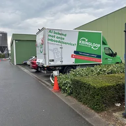 Groene bedrijfsbus van Kringloop met tekst 'Al bekend met onze inboedelservice?' en logo op parkeerterrein