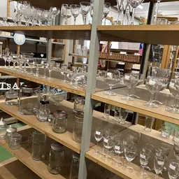 Glazen serviesgoed en drinkglazen uitgestald op houten schappen in een kringloopwinkel