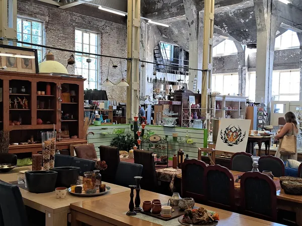 Spacieus interieur van kringloopwinkel met houten meubilair, zithoeken en grote ramen boven.