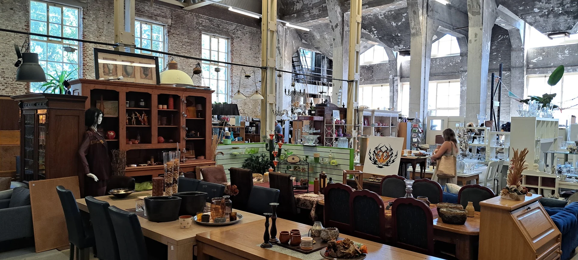 Spacieus interieur van kringloopwinkel met houten meubilair, zithoeken en grote ramen boven.