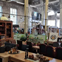 Spacieus interieur van kringloopwinkel met houten meubilair, zithoeken en grote ramen boven.