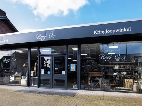 Donkerblauwe gevel van kringloopwinkel met grote ramen en winkelnaam op het uithangbord