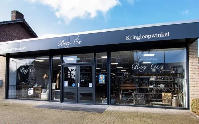 Donkerblauwe gevel van kringloopwinkel met grote ramen en winkelnaam op het uithangbord