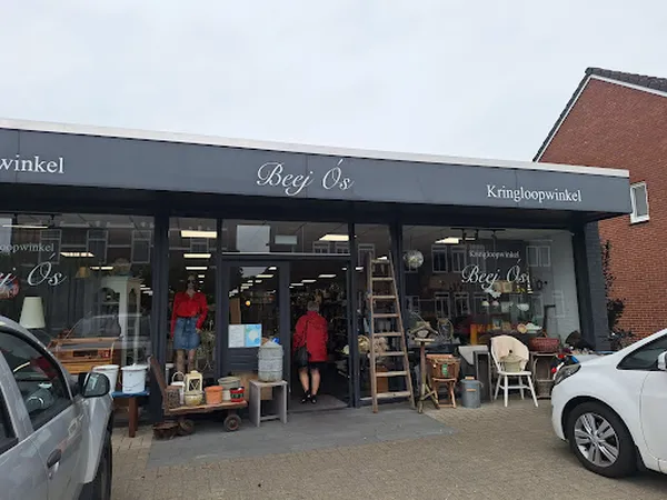 Gevel van kringloopwinkel Beej Ós met donkerblauwe pui, grote ramen, en zichtbare winkeluitstalling met meubels en spullen.