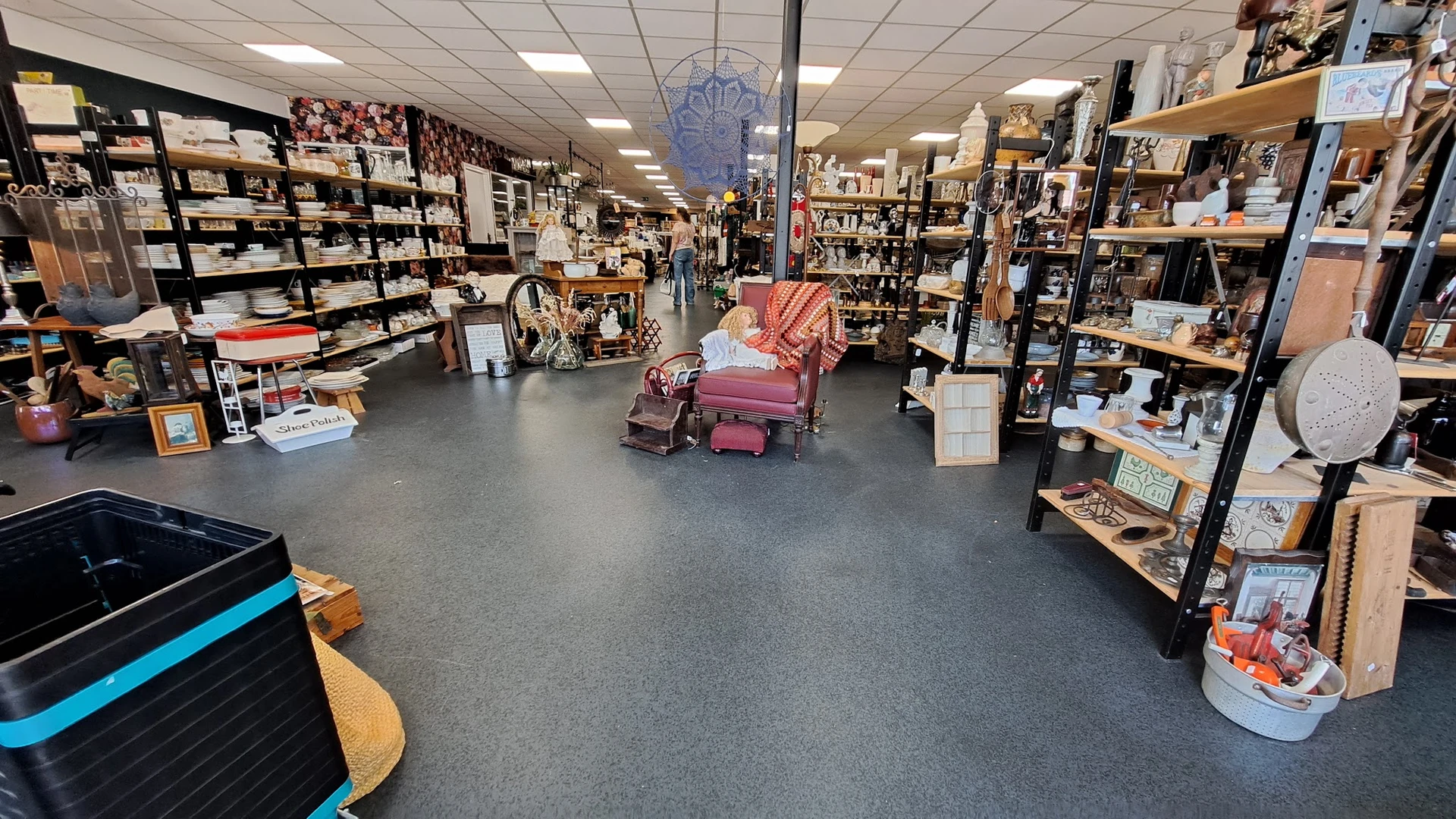Ruim winkelinterieur met stellingen vol spullen, een roze fauteuil in het midden en grijze vloer