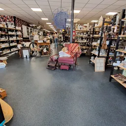 Ruim winkelinterieur met stellingen vol spullen, een roze fauteuil in het midden en grijze vloer