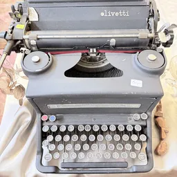 Grijze typemachine van bovenaf gefotografeerd met zichtbaar toetsenbord en papierrollen