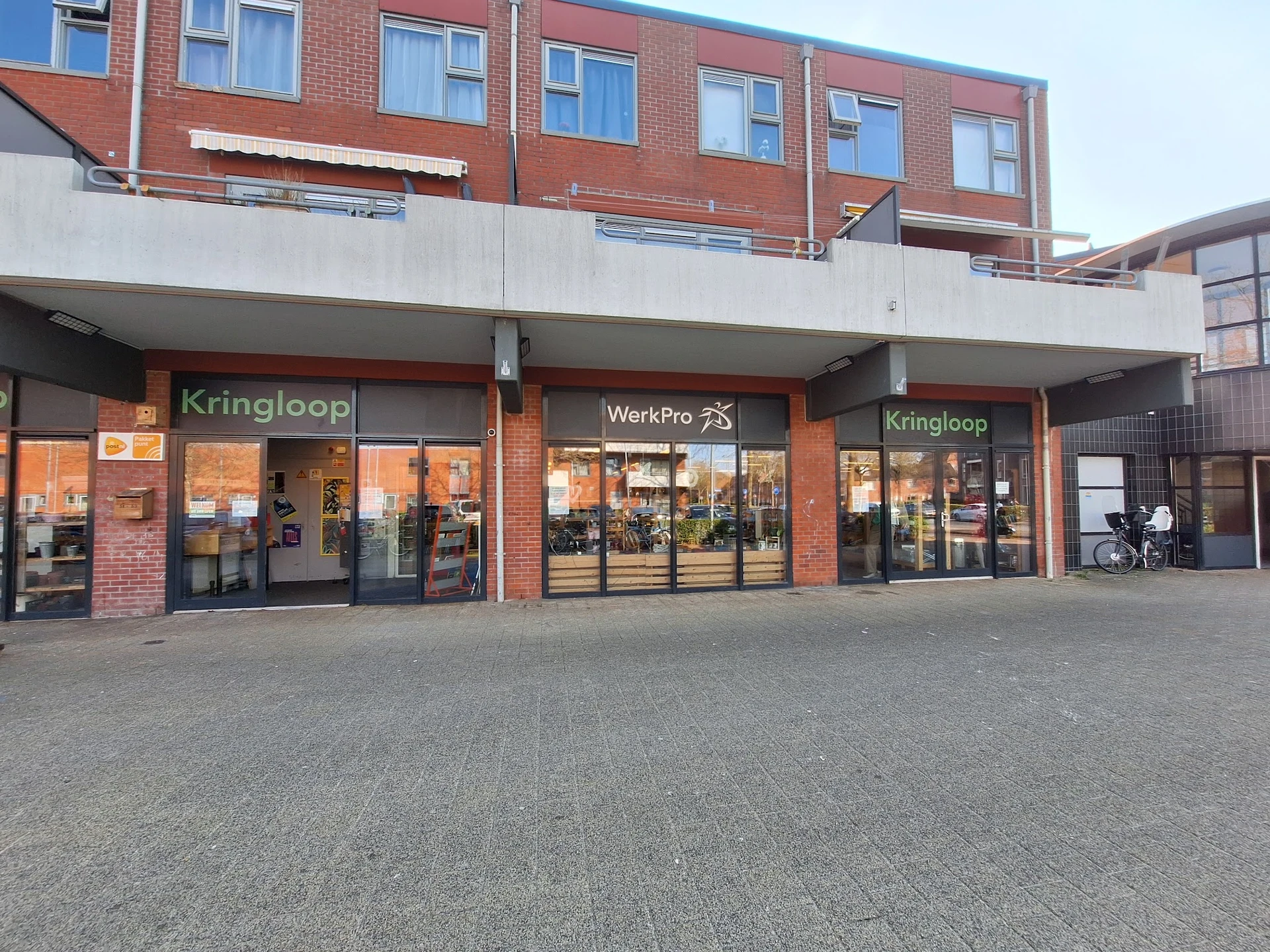 Gevel van kringloopwinkel met rode bakstenen, uitstalkramen en winkelnaam zichtbaar
