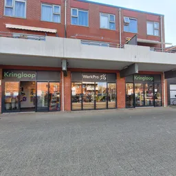 Gevel van kringloopwinkel met rode bakstenen, uitstalkramen en winkelnaam zichtbaar