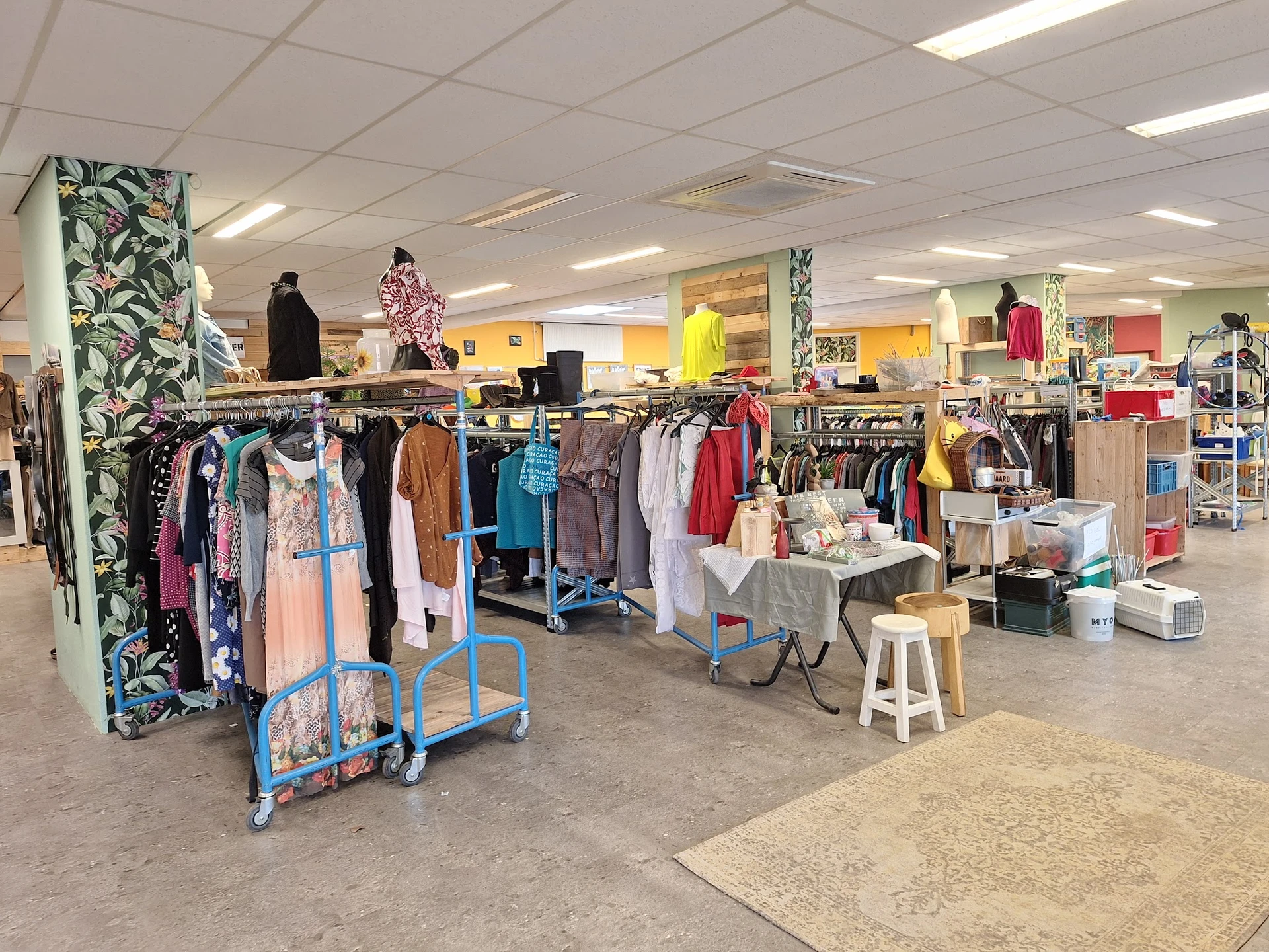 Overzicht van de winkelvloer met kledingrekken, uitgestalde tweedehands kleding en diverse artikelen