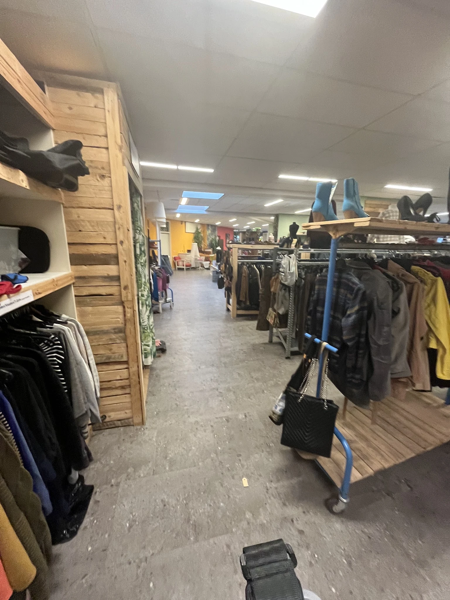 Winkelvloer met kledingrekken en houten kastenwand in kringloopwinkel
