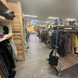 Winkelvloer met kledingrekken en houten kastenwand in kringloopwinkel