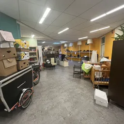 Winkelvloer van kringloopwinkel met stellingen, dozen, fietsen en diverse spullen tegen gekleurde wanden