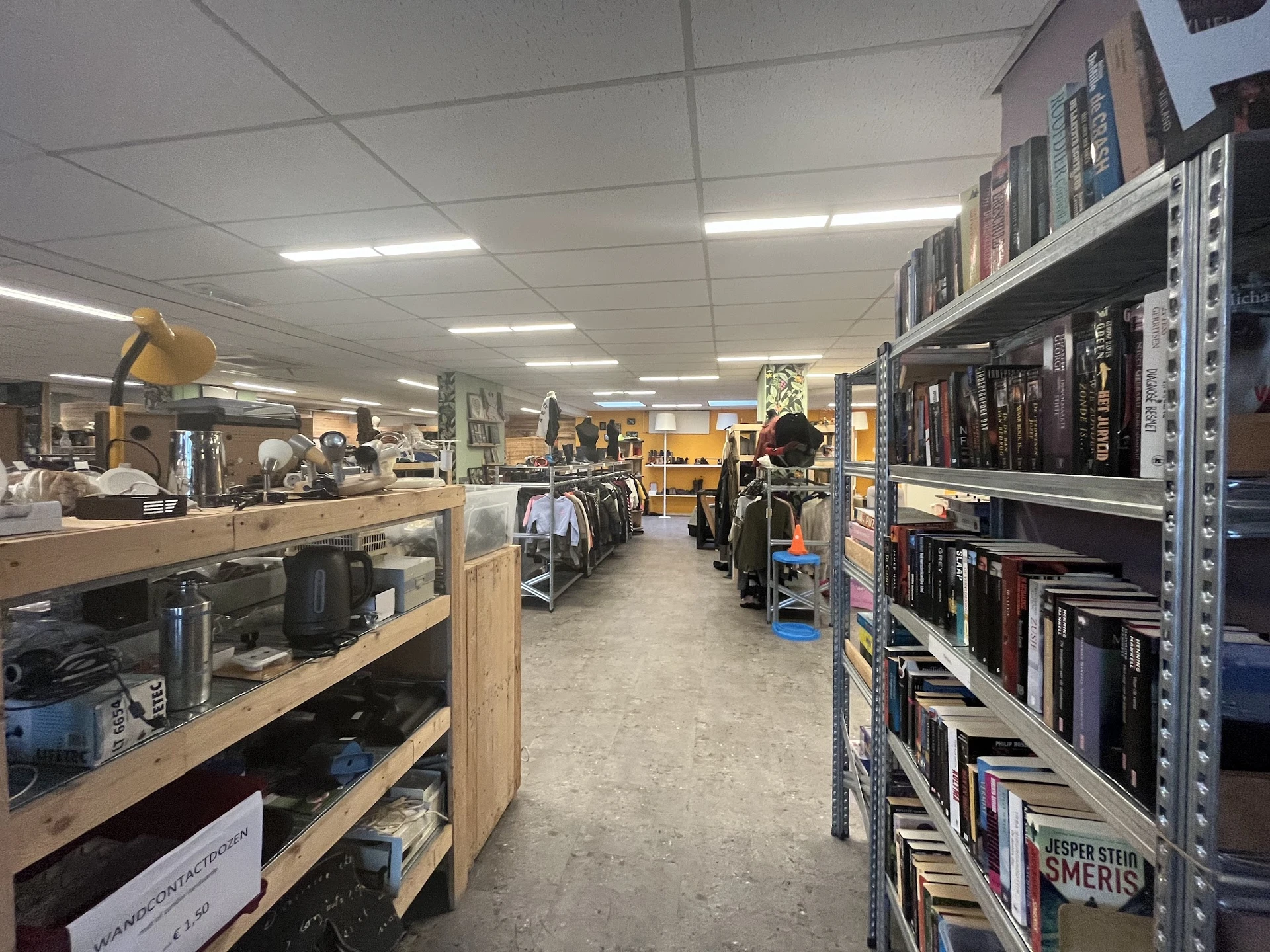 Winkelvloer met stellingen vol boeken, kleding op hangers en diverse spullen uitgestald