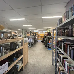 Winkelvloer met stellingen vol boeken, kleding op hangers en diverse spullen uitgestald