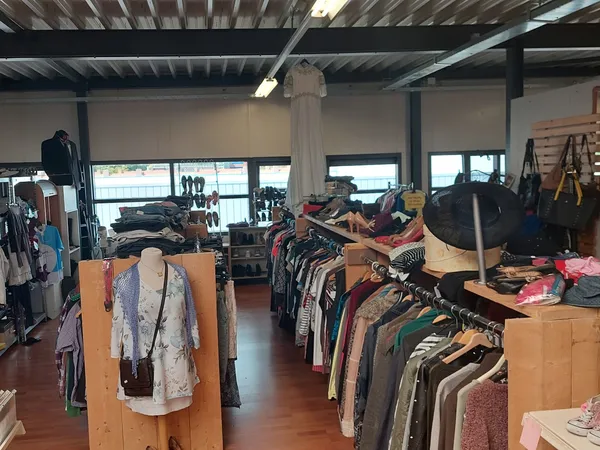 Winkelinterieur met kledingrekken, dozen met kleding en diverse tweedehandsartikelen langs de wanden