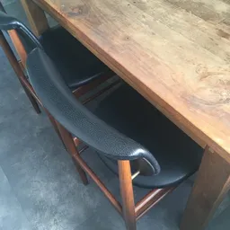 Zwarte lederen stoel met houten poten naast houten tafel